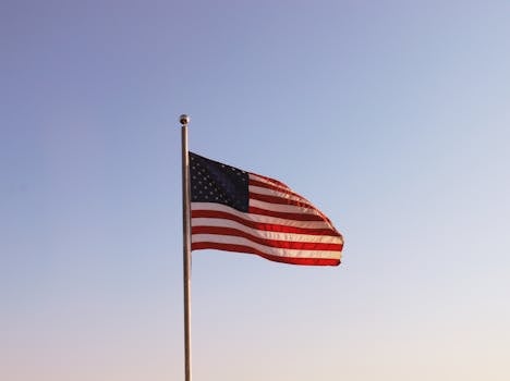 A United States flag waving on a flagpole against a clear blue sky, symbolizing patriotism.